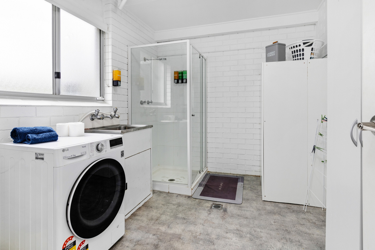 This downstairs bathroom and laundry combines a shower, toilet and washing space for the lower level of Skye’s Beach House.