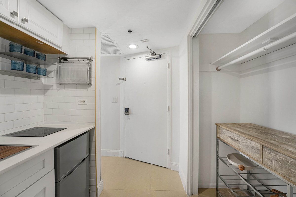The entry hall passes the kitchen to a full closet with hangers, an iron and ironing board, plus beach chairs and a rolling cooler for the sand.