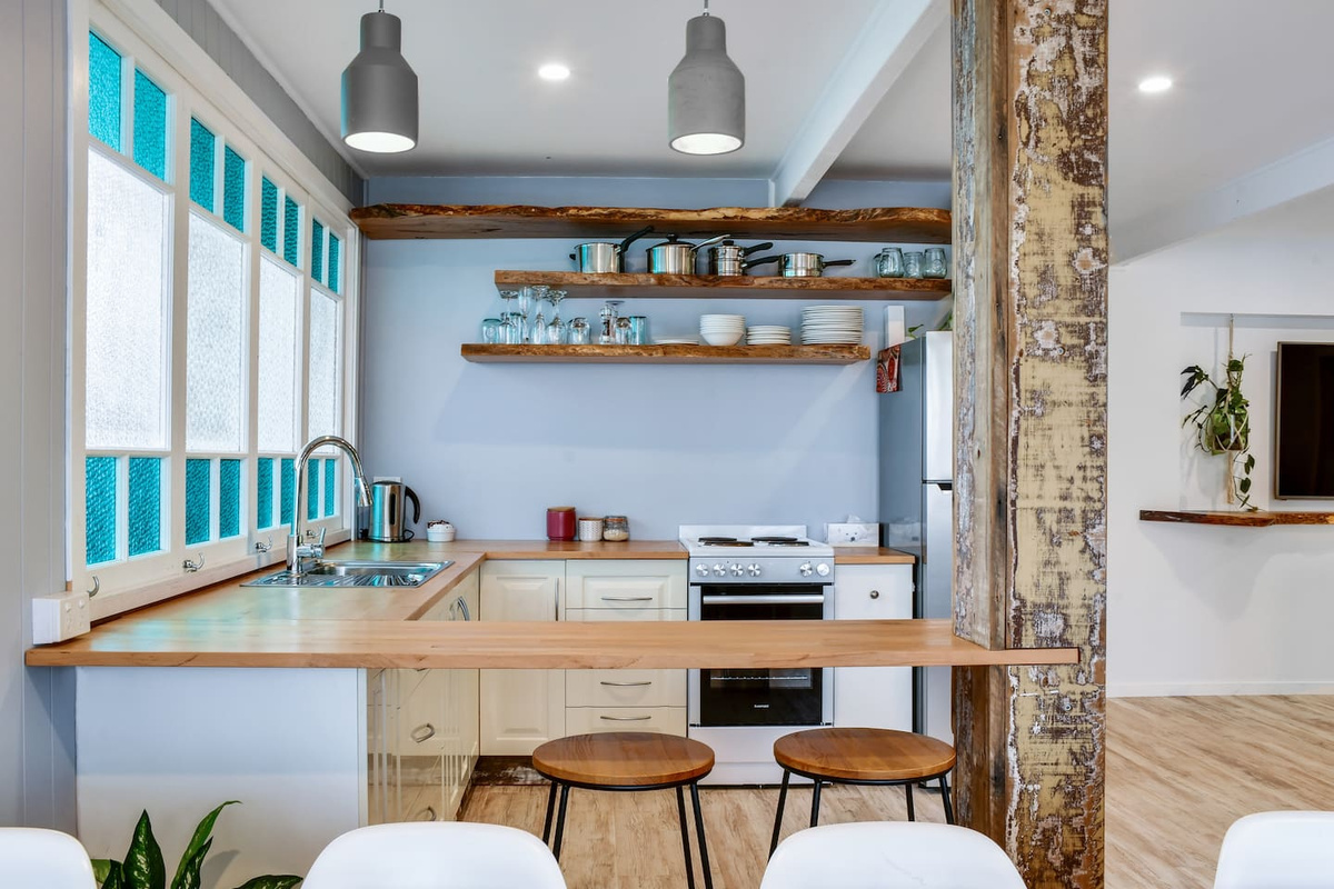 Exposed timber beams, aqua-framed windows and natural wood finishes give the kitchen at Aaron's Beachside Boat House a distinctive beach-house personality.