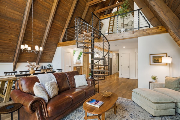 From the living and dining area you can access the 2nd floor loft and primary bedroom using this modern spiral staircase. This view also shows the 3rd floor loft space accessible with the vintage library ladder.