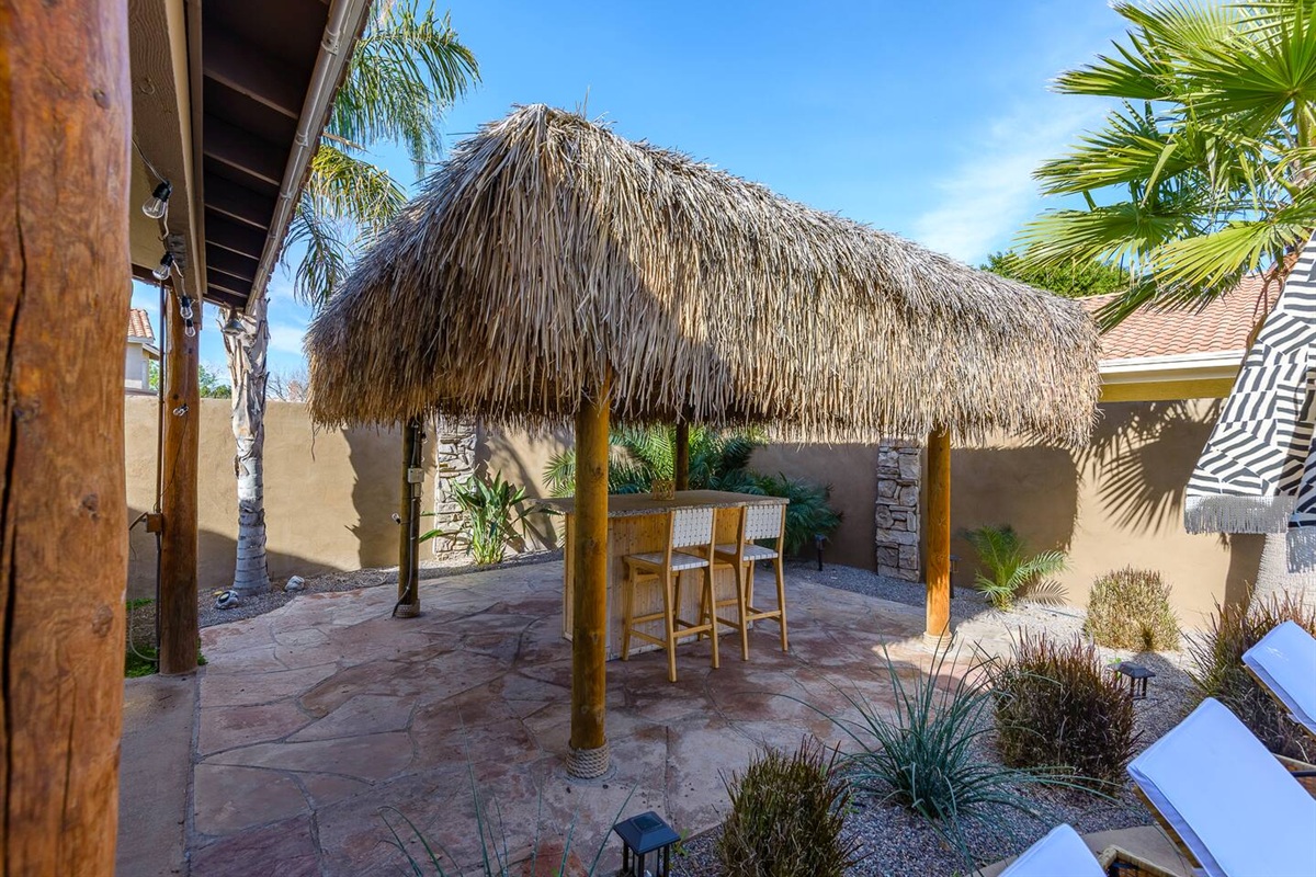 Outdoor tiki pergola lounge with bar seating, ceiling fan, and a shaded spot to relax by the pool.