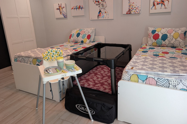 Kids' bedroom at Villa Coral featuring twin beds, colorful animal wall art, a set up Graco Pack 'n Play crib, a high chair, and toddler dinnerware in Dorado, Puerto Rico.