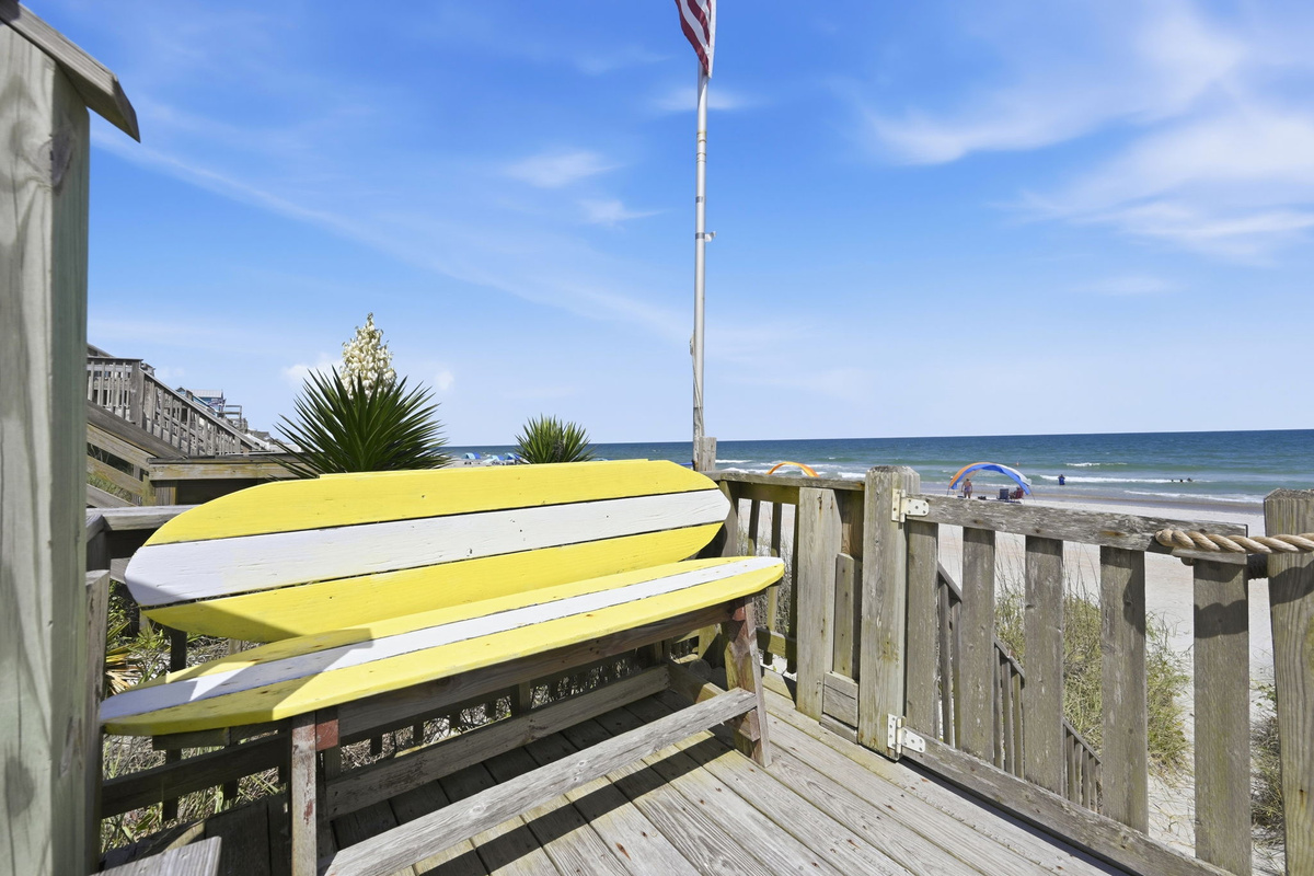 Elevated beachside hangout with colorful surfboard bench and ocean backdrop