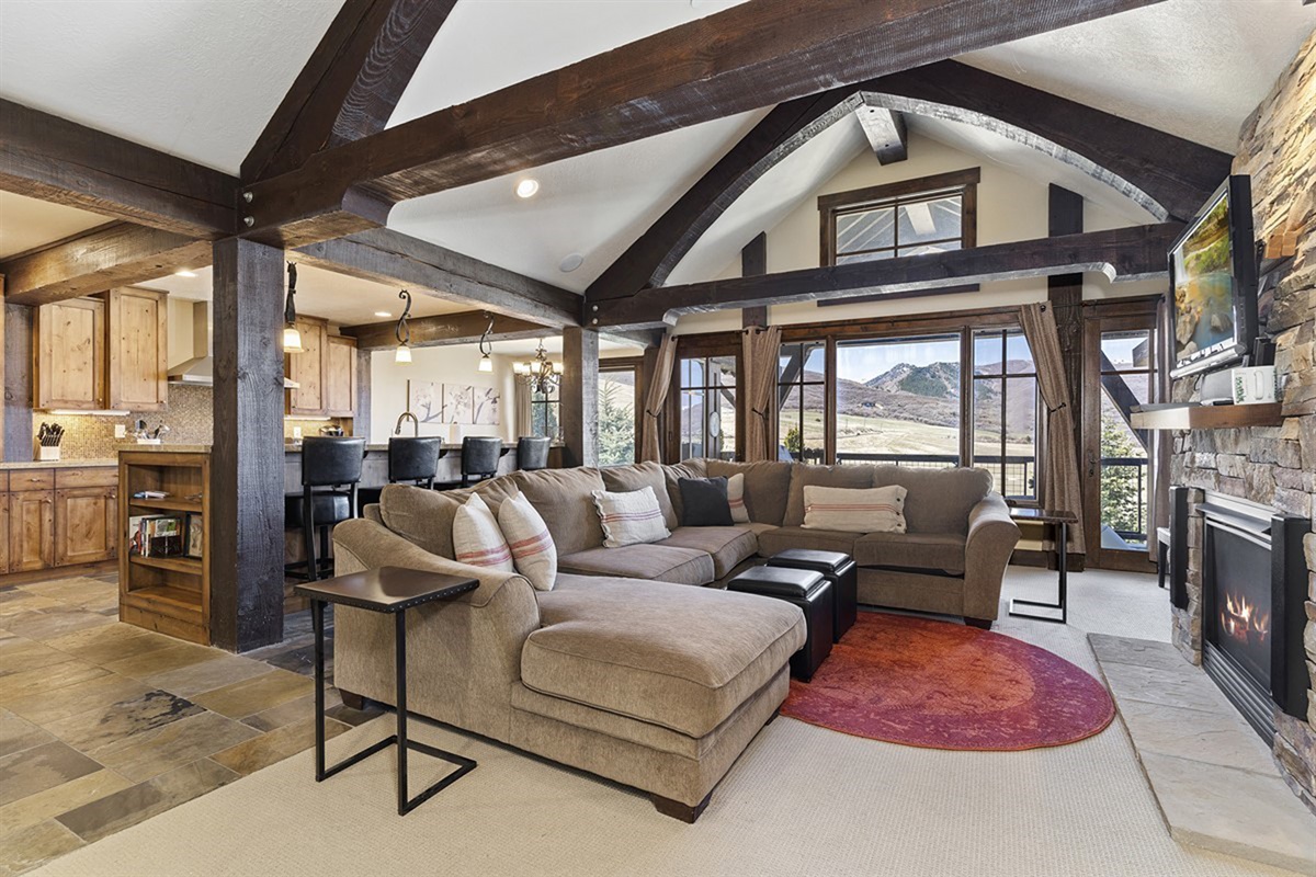 A grand main living space defined by soaring vaulted ceilings, exposed timber beams, and expansive windows—offering an elegant yet inviting atmosphere framed by breathtaking mountain views.