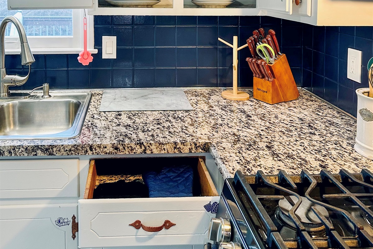 Kitchen drawer with oven mitts and trivets, and cabinets stocked with full sets of large and small plates and bowls, neatly organized and ready for everyday dining.