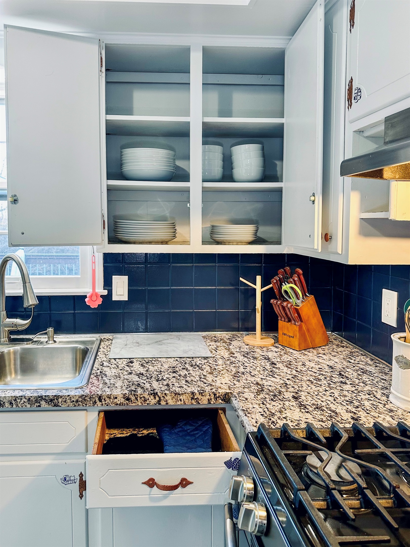 Kitchen drawer with oven mitts and trivets, and cabinets stocked with full sets of large and small plates and bowls, neatly organized and ready for everyday dining.