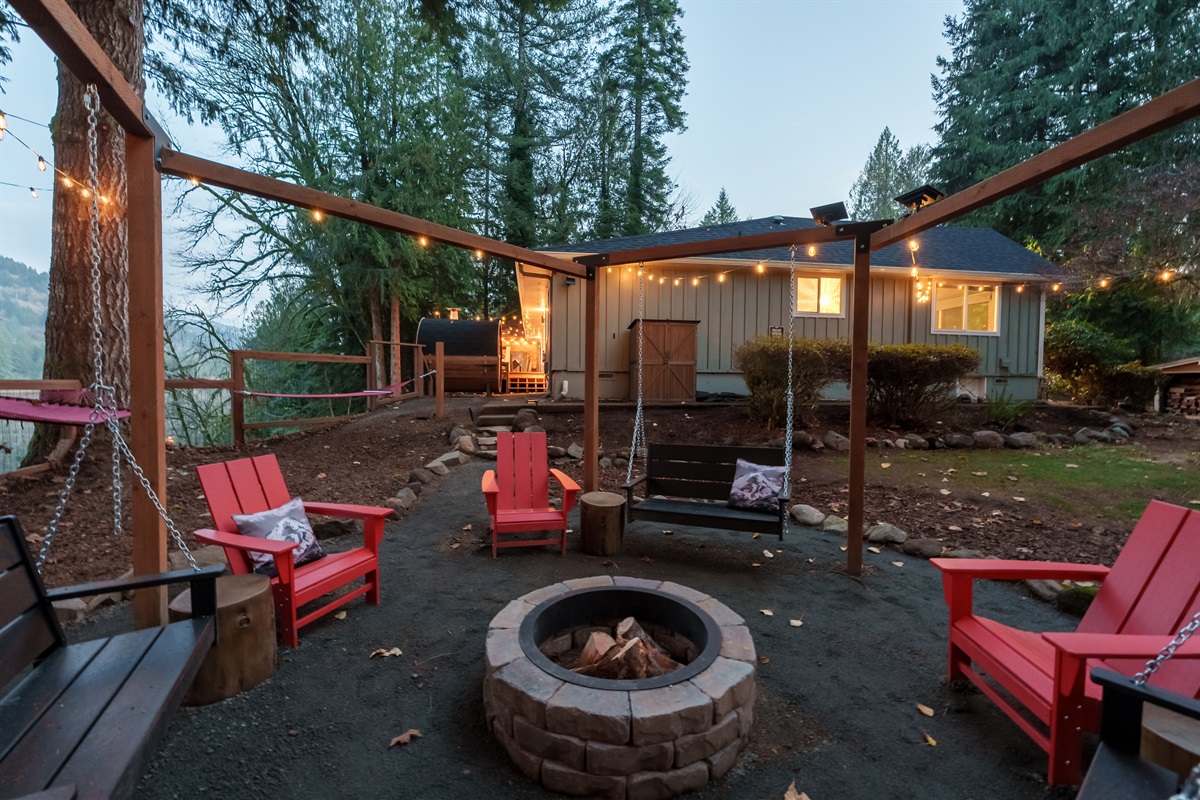 Gather around the glowing fire pit beneath string lights, with swings and Adirondack chairs creating the perfect spot for s’mores, stories, and peaceful forest evenings.
