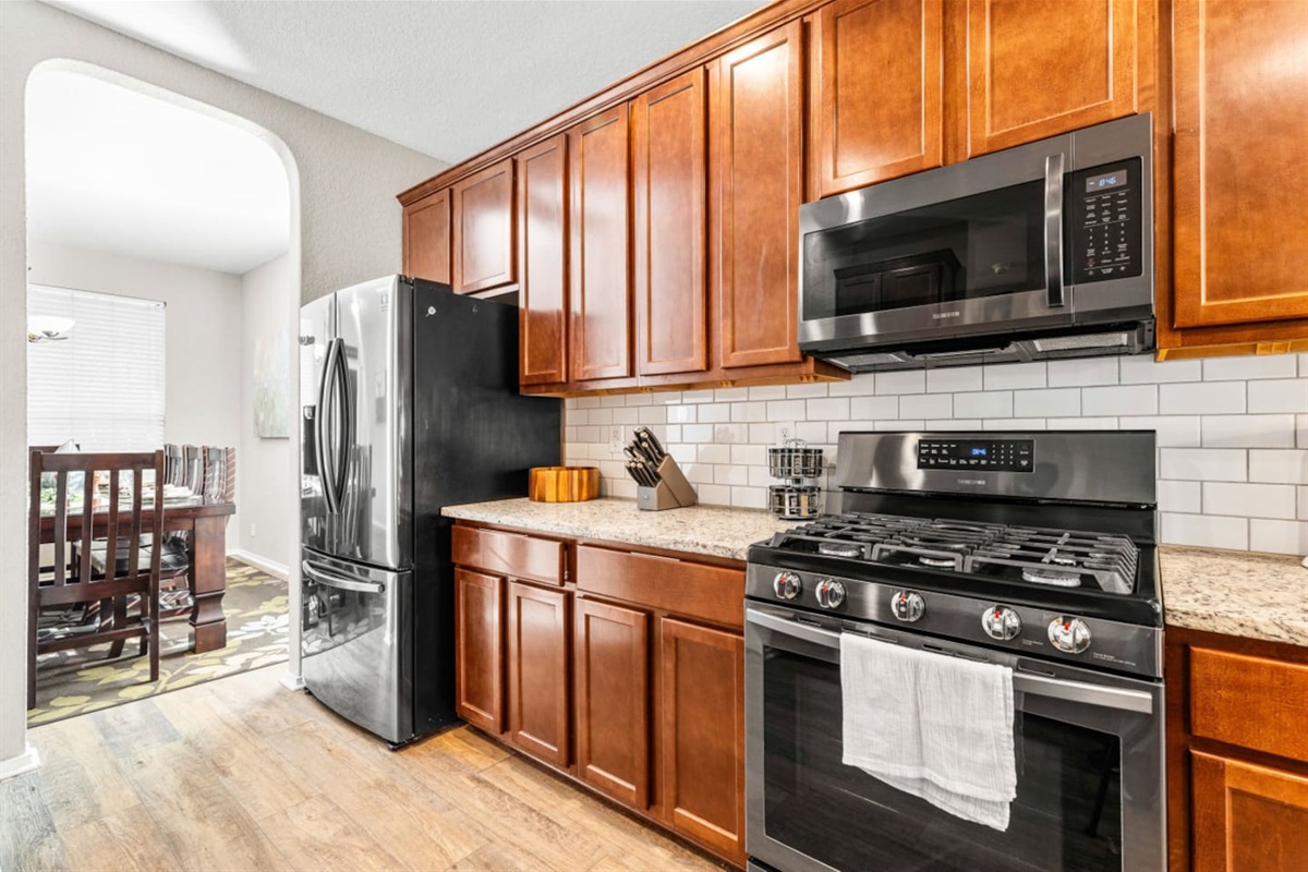 Spacious kitchen with full fridge/freezer combo, stainless steel oven, microwave, gas cooktop, and all cooking tools, pots, pans, dishes, and cutlery included.