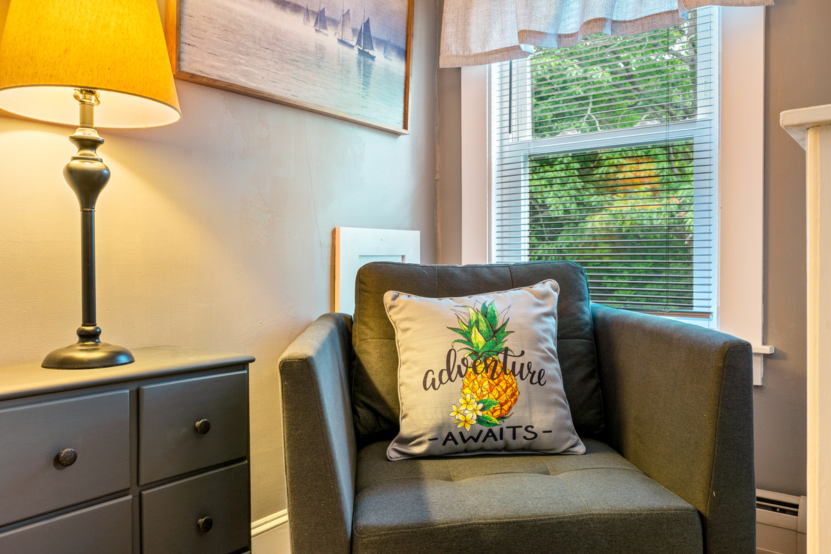 Serving as a private architectural buffer, The Pebble Nook features independent doors to both the landing and the queen suite. With an armchair, dresser, and wooded window view, it functions as a flexible dressing room or a quiet retreat.