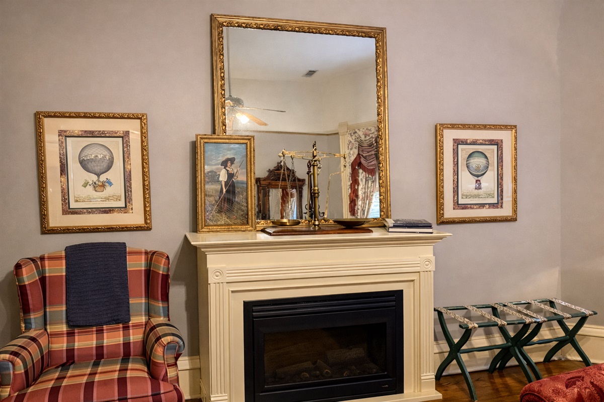 Decorative fireplace with framed artwork, large mirror, and classic Victorian seating.