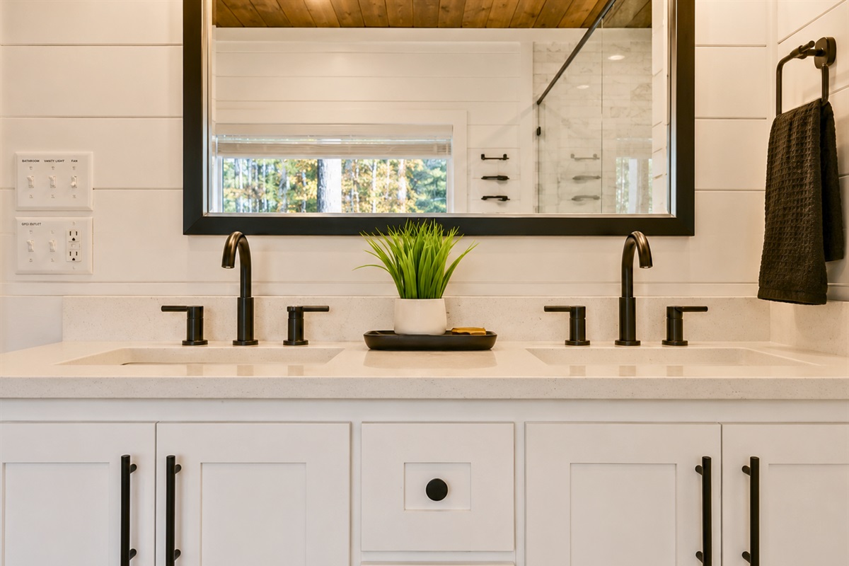 Dual vanities with sleek black fixtures and farmhouse-inspired details add both comfort and style to the relaxing bathroom space.