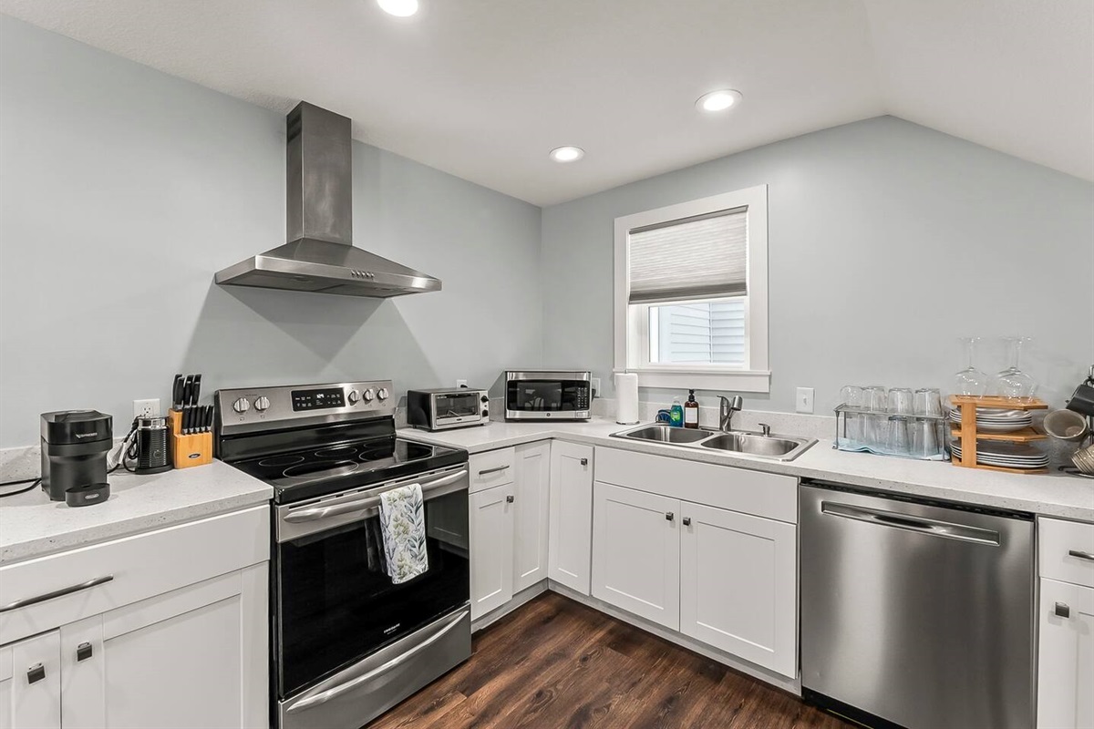 Bright corner kitchen with electric range, stainless hood, dishwasher, and plenty of counter space for everyday cooking.