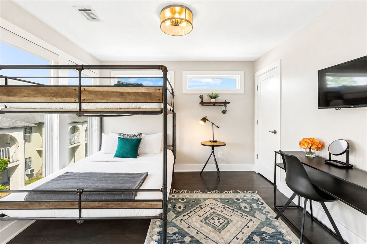 Industrial style queen over queen bunk bed, styled in cozy neutrals - Bright room with oversized windows, geometric rug, and desk setup for work or study - Thoughtful decor with greenery, light wood accents, and clean minimalist lines