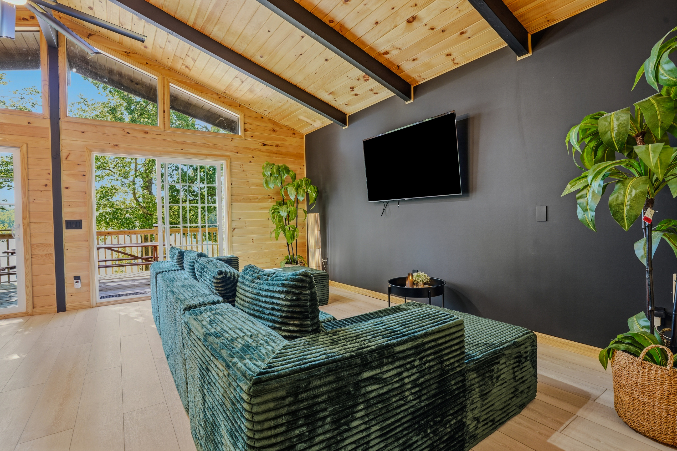 Living room from the secondary angle — teal sectional, wood-paneled walls, and floor-to-ceiling windows