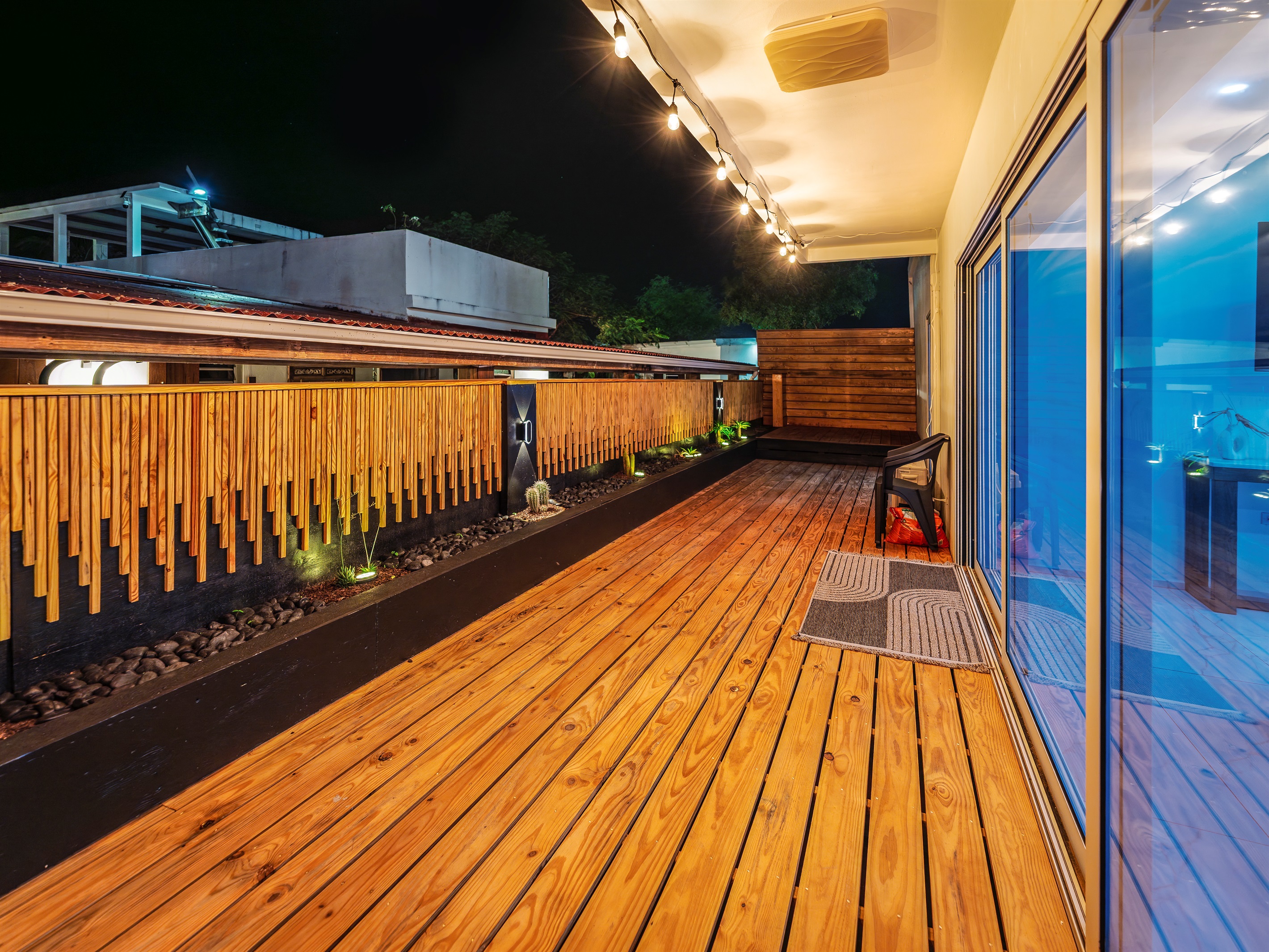 Wide night-time view of the wooden deck with string lights and planters