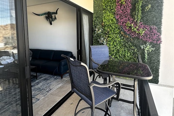Step from the cozy living room to the balcony, featuring a stylish high-top outdoor dining table and a serene outdoor nature wall.