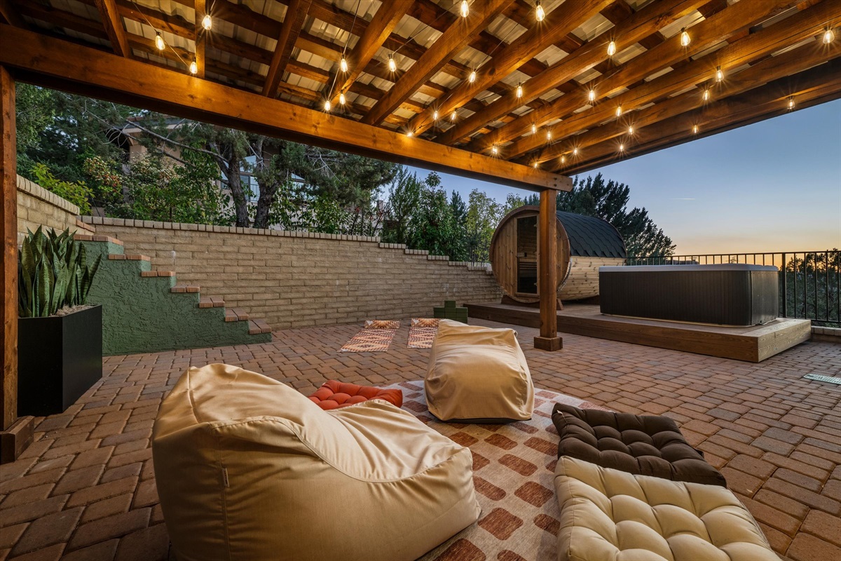A spa-like outdoor escape featuring a private hot tub, barrel sauna, and cozy lounge space under ambient lighting.