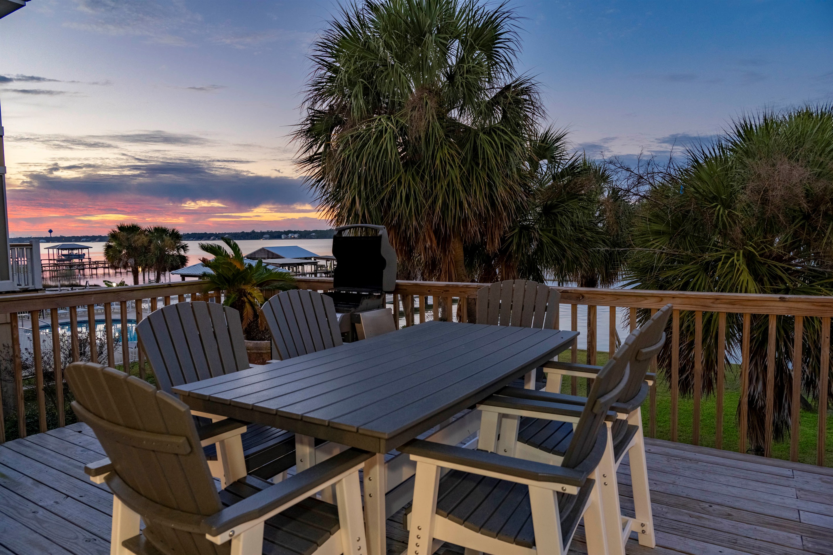 Relaxing lakeside deck with sunset, palm trees, and cozy outdoor dining vibes.
