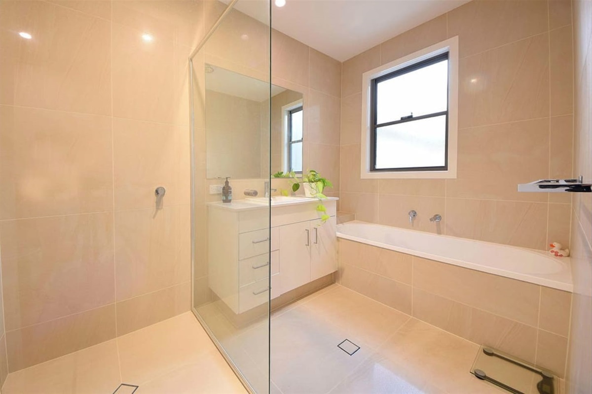 Bright bathroom with a glass-enclosed shower, vanity, and soaking tub, offering a luxurious experience.