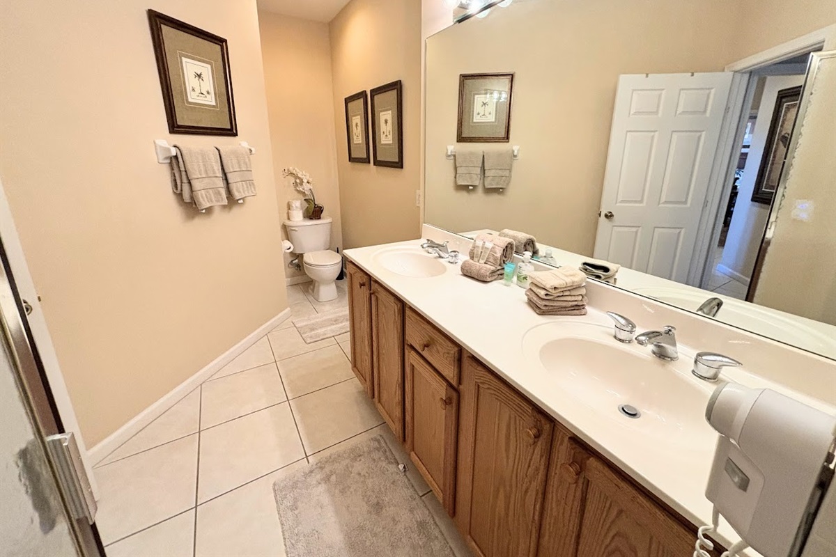 Spacious bathroom featuring a double-sink vanity, large mirror, tile flooring, and clean neutral finishes.