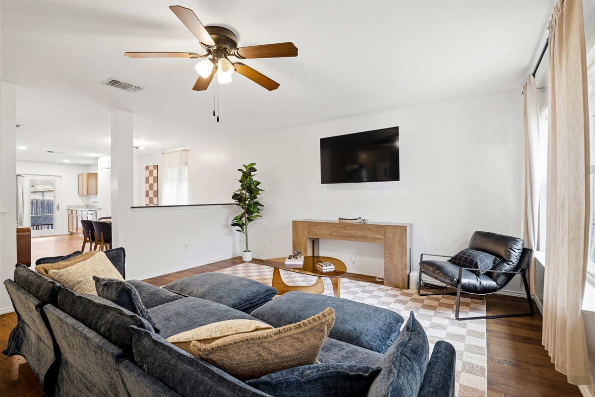 Open living area with wall-mounted Smart TV, plush sectional sofa, ceiling fan, and natural light. Comfortable space for movie nights, streaming, and unwinding after a day at SeaWorld or Six Flags.