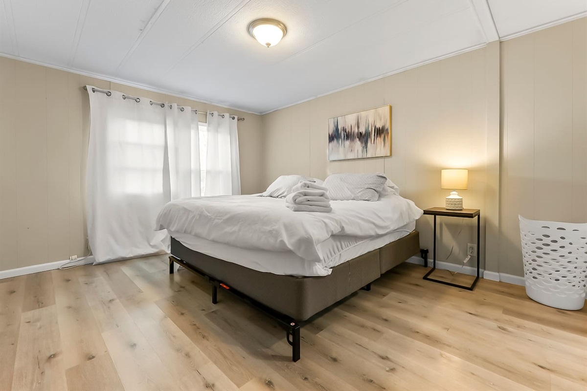 Spacious bedroom with a king-size bed, soft lighting, and natural sunlight from large windows.