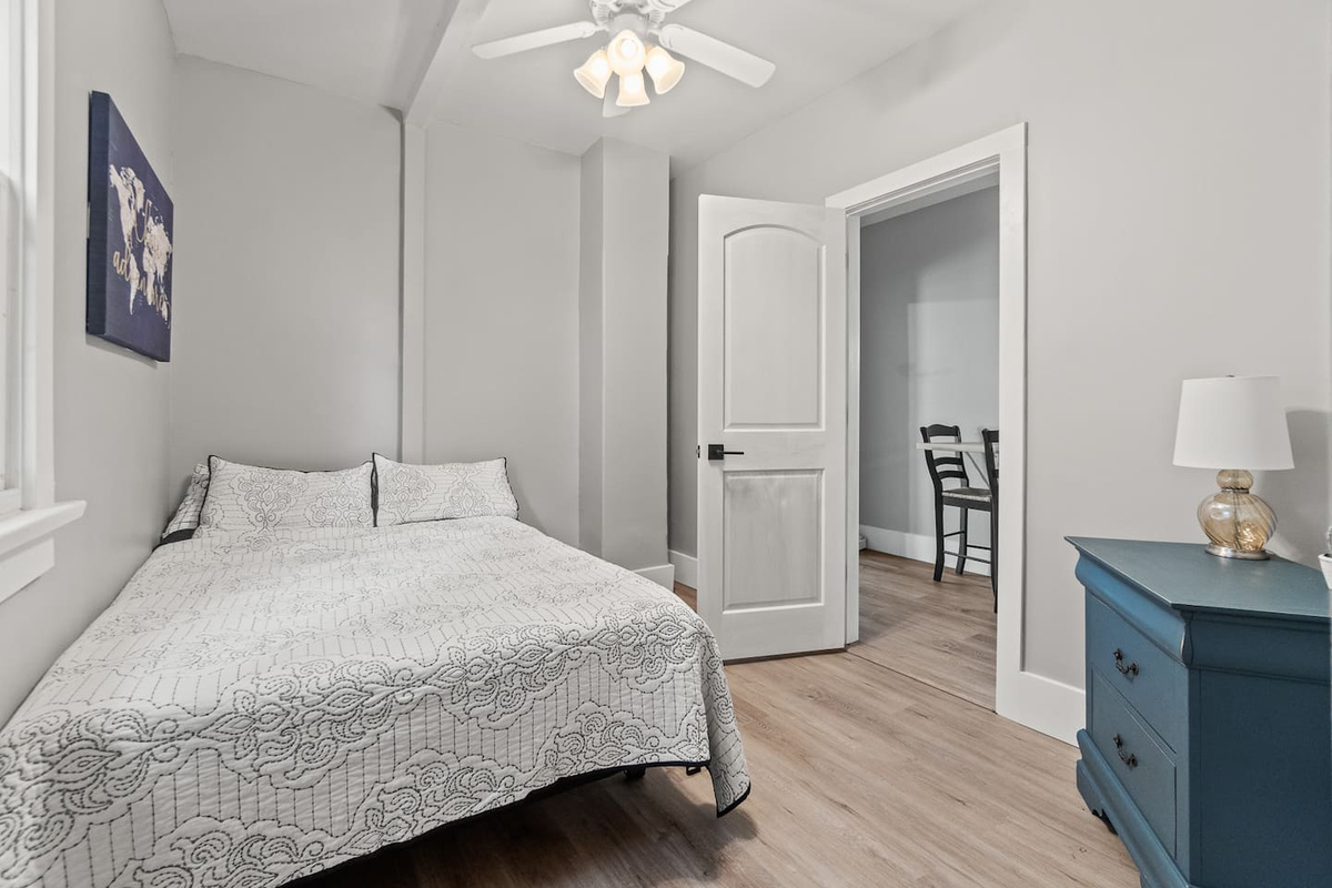 Double bed with ceiling fan, hardwood floors, and natural light.