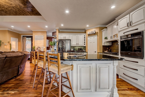 Full kitchen with white cabinets, granite island, bar seating and stainless appliances