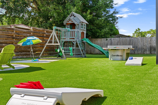 Non-stop backyard entertainment! This angle showcases our cornhole game boards ready for action, with the premium wooden playset, sand bunker area, and Cornilleau ping-pong table spread across the beautiful artificial turf.