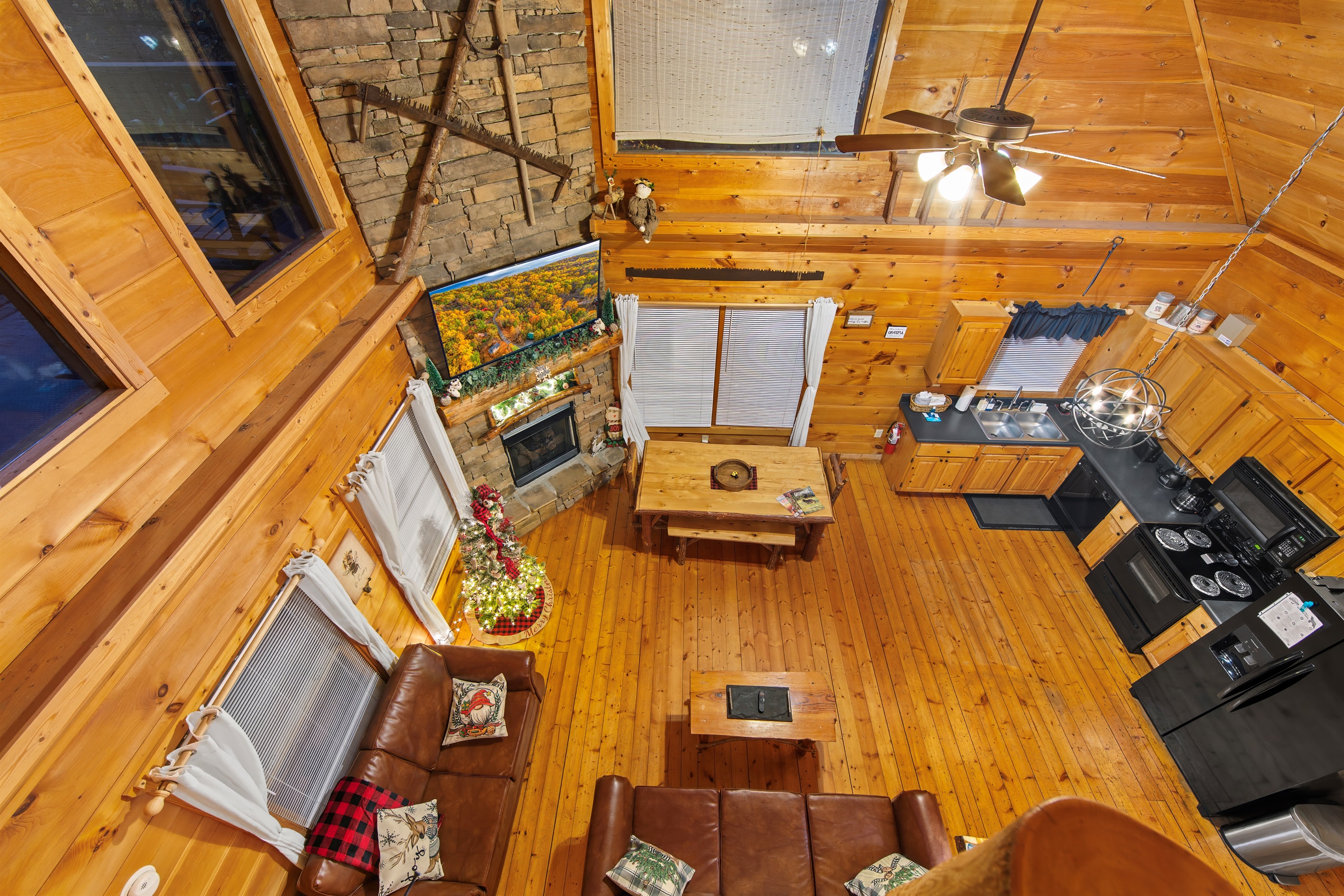 A charming cabin interior featuring an open living, dining and kitchen area. The wood-paneled walls and high ceilings create a warm atmosphere, complemented by leather seating and rustic design touches.