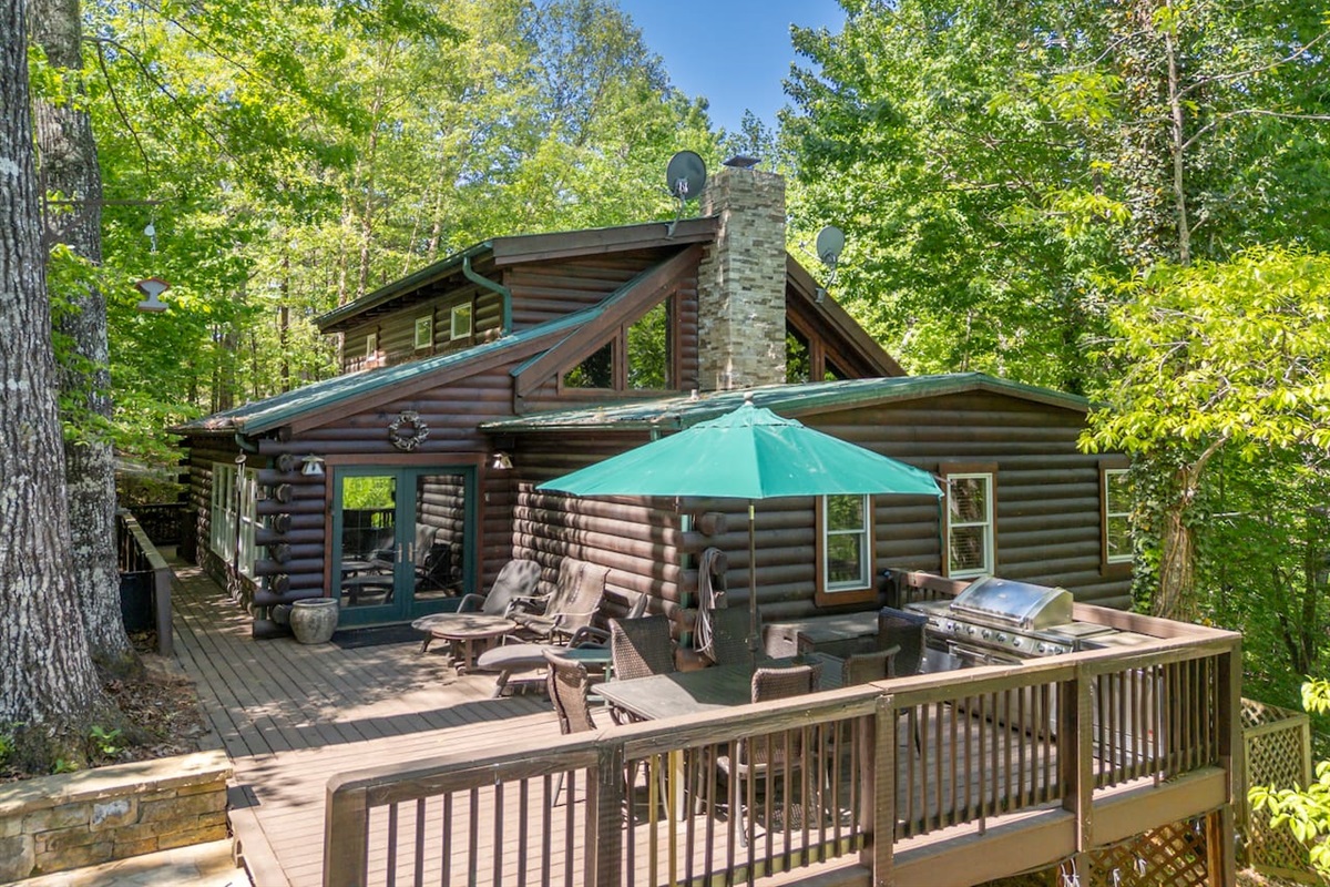 Spacious main-level deck surrounded by peaceful wooded views, outdoor seating, dining space, and a grill perfect for relaxing, entertaining, and enjoying fresh mountain air.