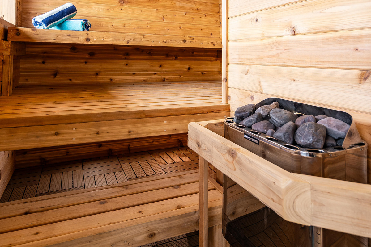 Warm wood-paneled sauna featuring tiered bench seating and a traditional stone heater.