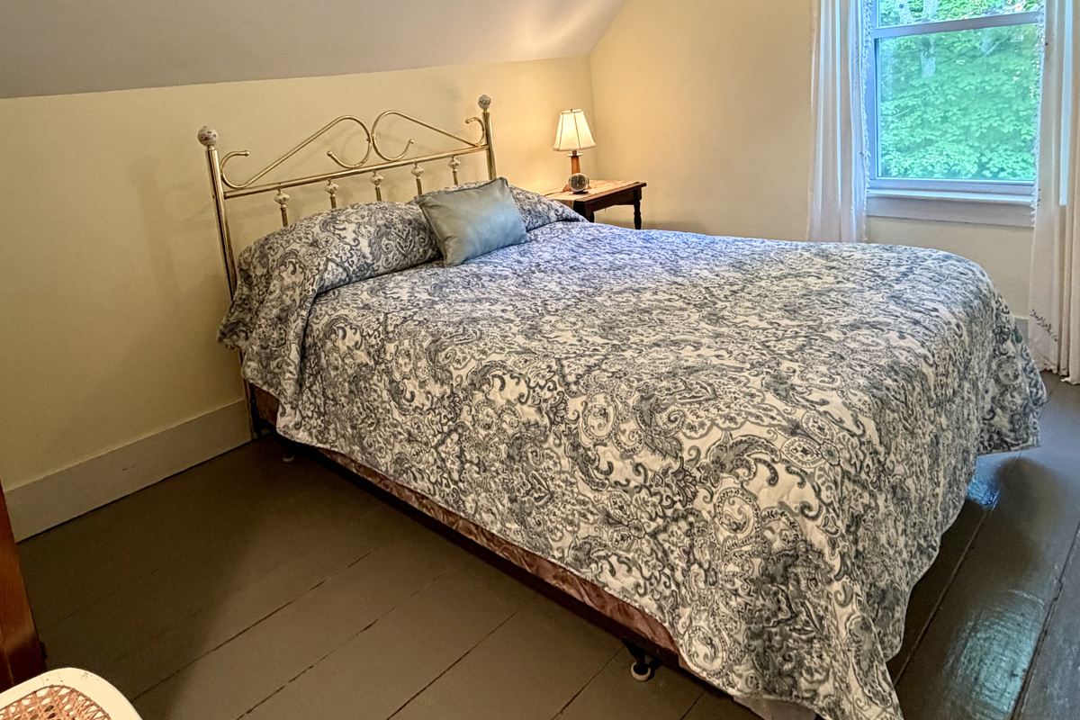A beautifully refreshed guest bedroom featuring a comfortable full bed with a classic brass frame and painted wood floors. Replacing the old twin layout opens up a wealth of space, offering a peaceful, airy retreat near Acadia.