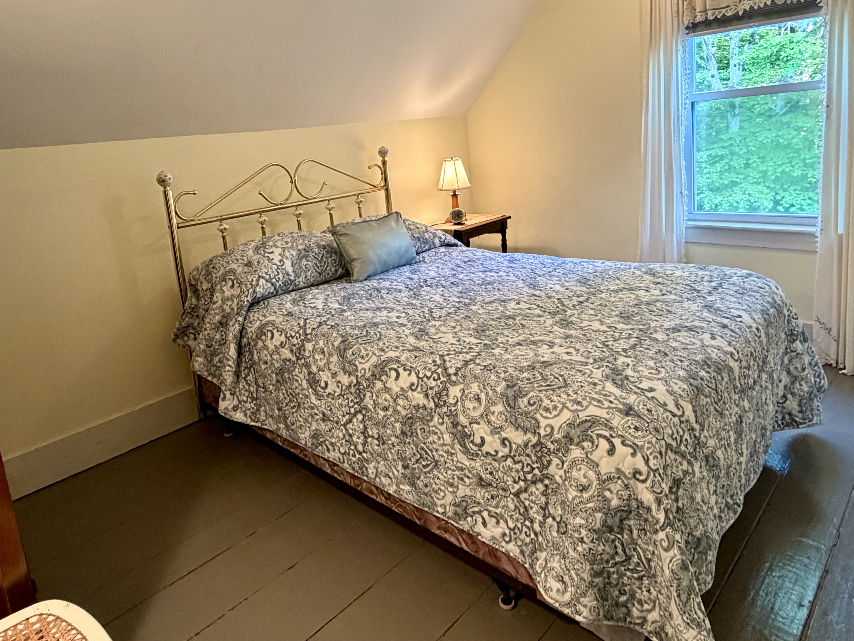 A beautifully refreshed guest bedroom featuring a comfortable full bed with a classic brass frame and painted wood floors. Replacing the old twin layout opens up a wealth of space, offering a peaceful, airy retreat near Acadia.