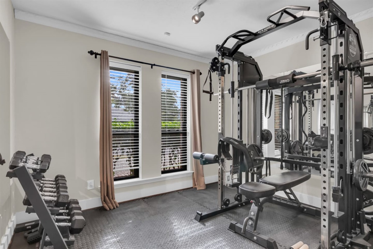 Private home gym equipped with a full weight rack, dumbbells, and strength-training equipment, offering a convenient space for workouts without leaving the house.