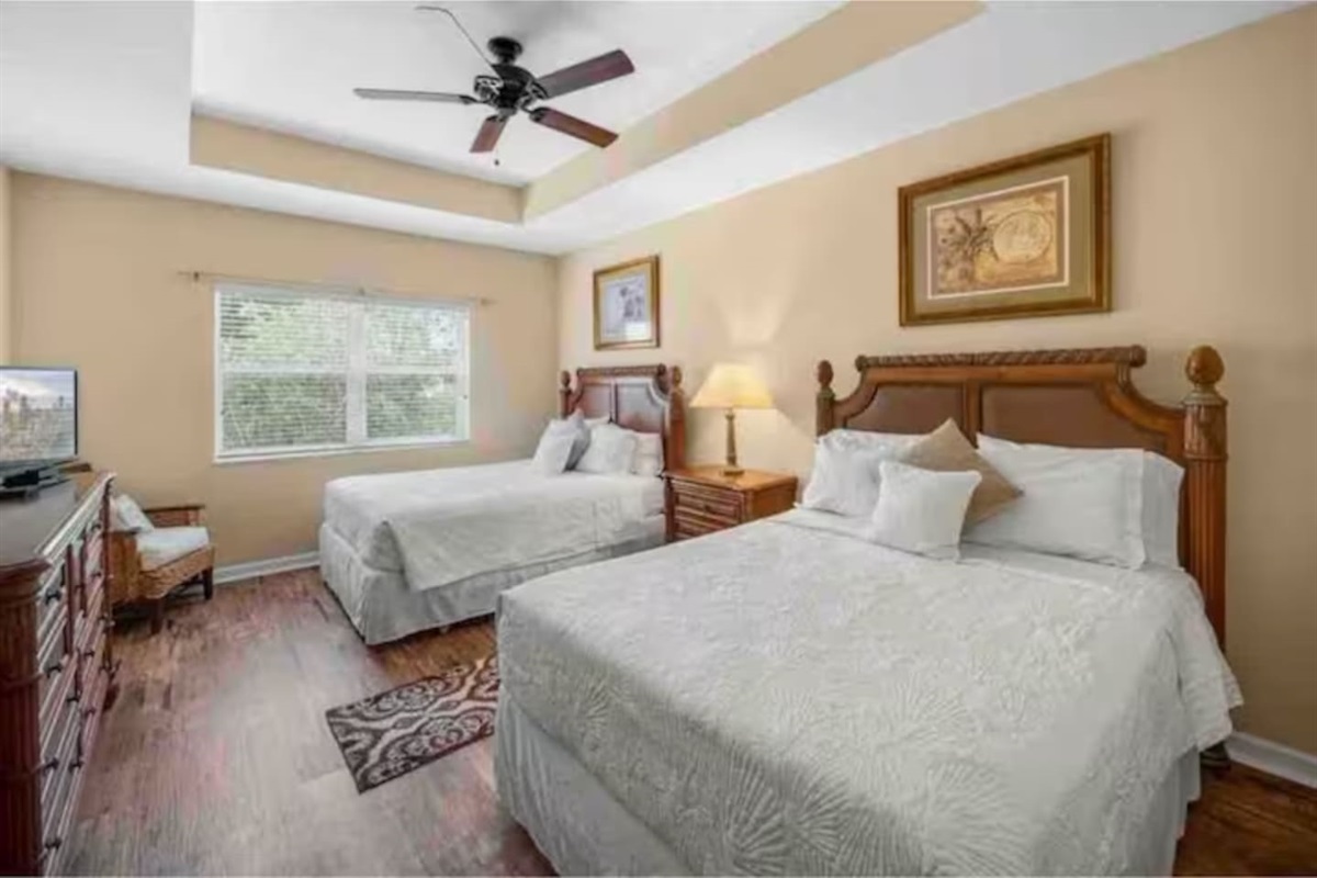 Comfortable bedroom featuring two beds, ceiling fan, dresser storage, and a bright, relaxing layout.