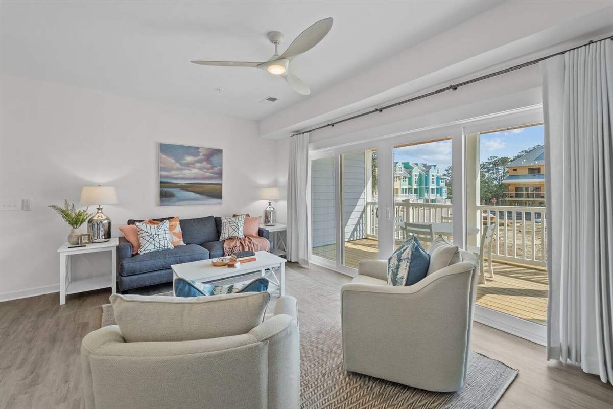 Primary living space with 3-seat couch, 2 swivel chairs, TV, and sliding glass doors to the private patio