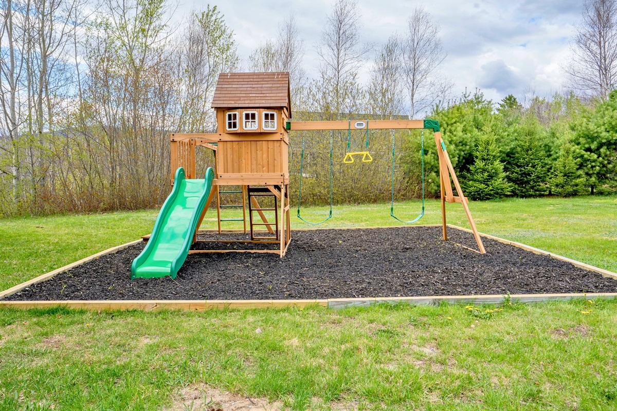 Fun awaits in the backyard with this charming playground set complete with swings and a slide, surrounded by peaceful nature views.
