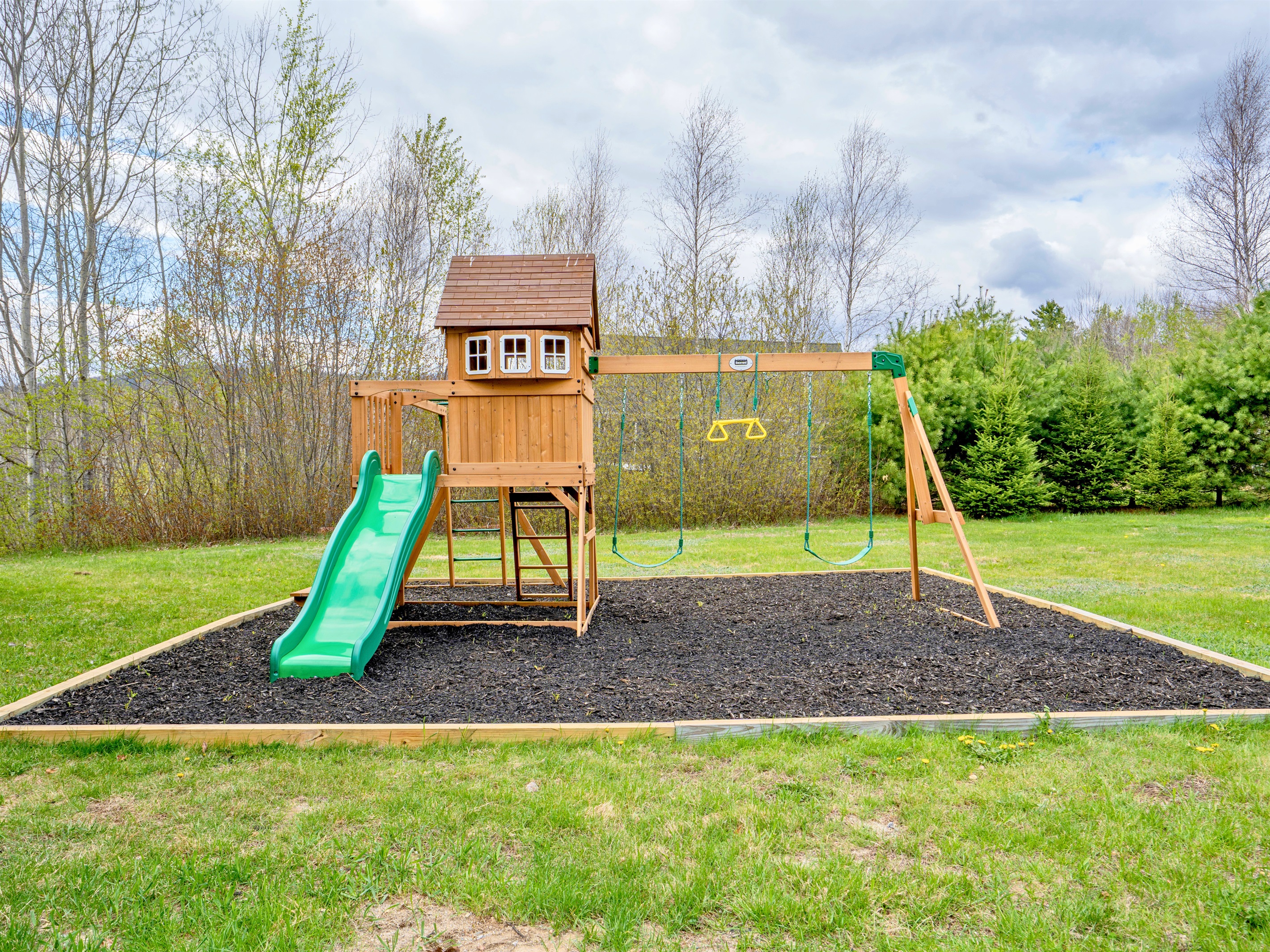 Fun awaits in the backyard with this charming playground set complete with swings and a slide, surrounded by peaceful nature views.