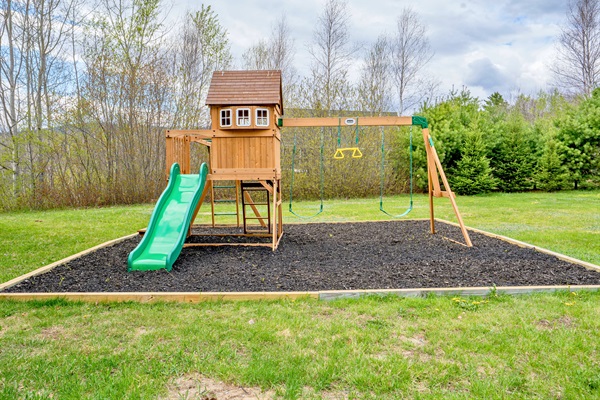 Fun awaits in the backyard with this charming playground set complete with swings and a slide, surrounded by peaceful nature views.