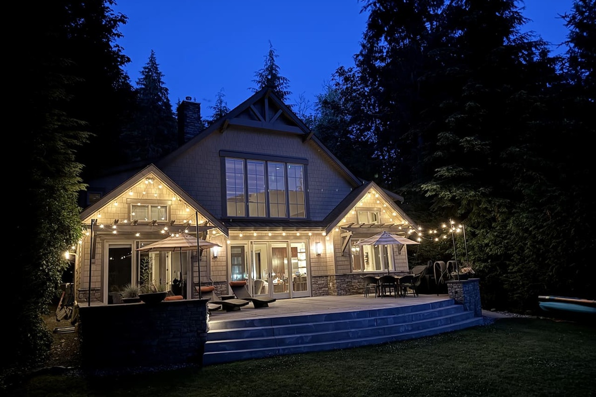 Twilight view of the house exterior, warmly lit by patio lights.