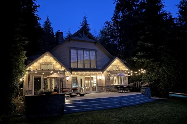 Twilight view of the house exterior, warmly lit by patio lights.