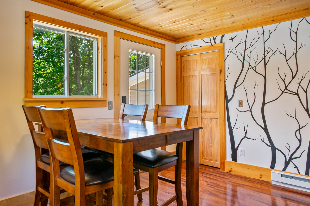 Step inside to the bright dining area within the eat-in kitchen. This space features a wooden dining table, a large window, a custom tree mural, and double wooden bifold doors opening to a spacious kitchen pantry closet for food storage.