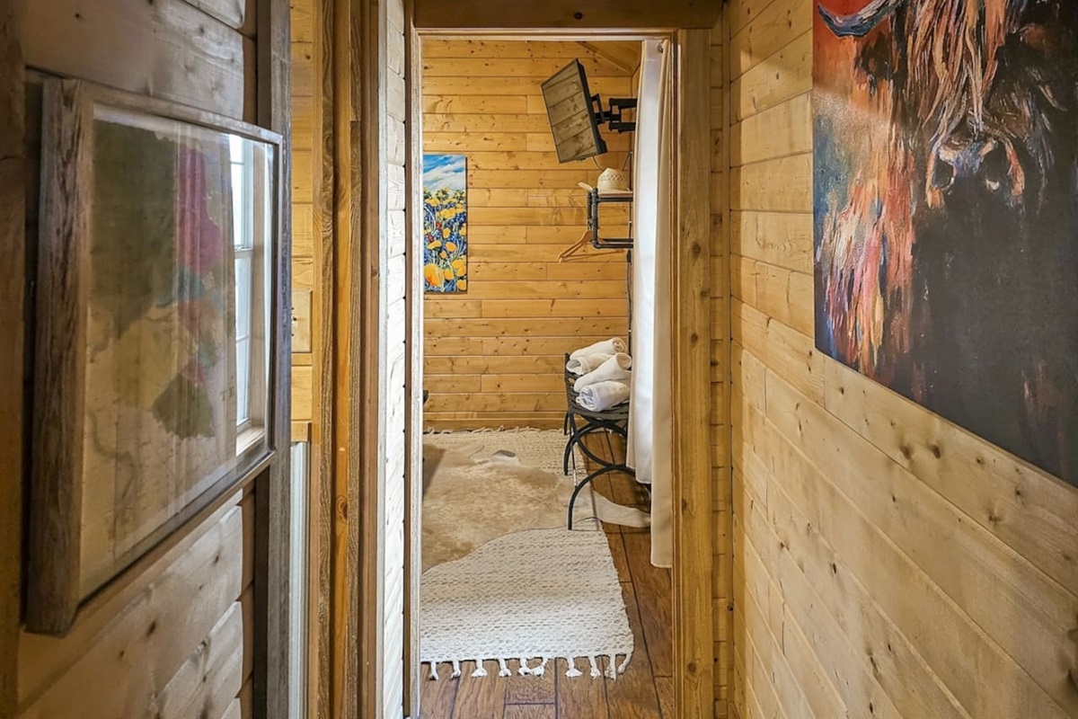 This cozy hallway leads you to a welcoming bedroom, adorned with rustic art that captures the spirit of the Texas Hill Country.