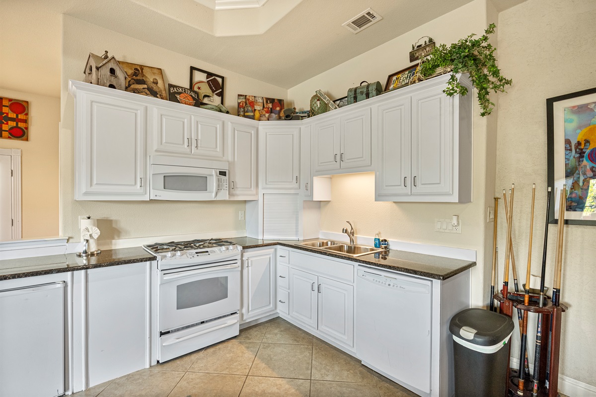 Compact kitchenette in the game room area with mini fridge, microwave, sink, and essential prep space for snacks and drinks.