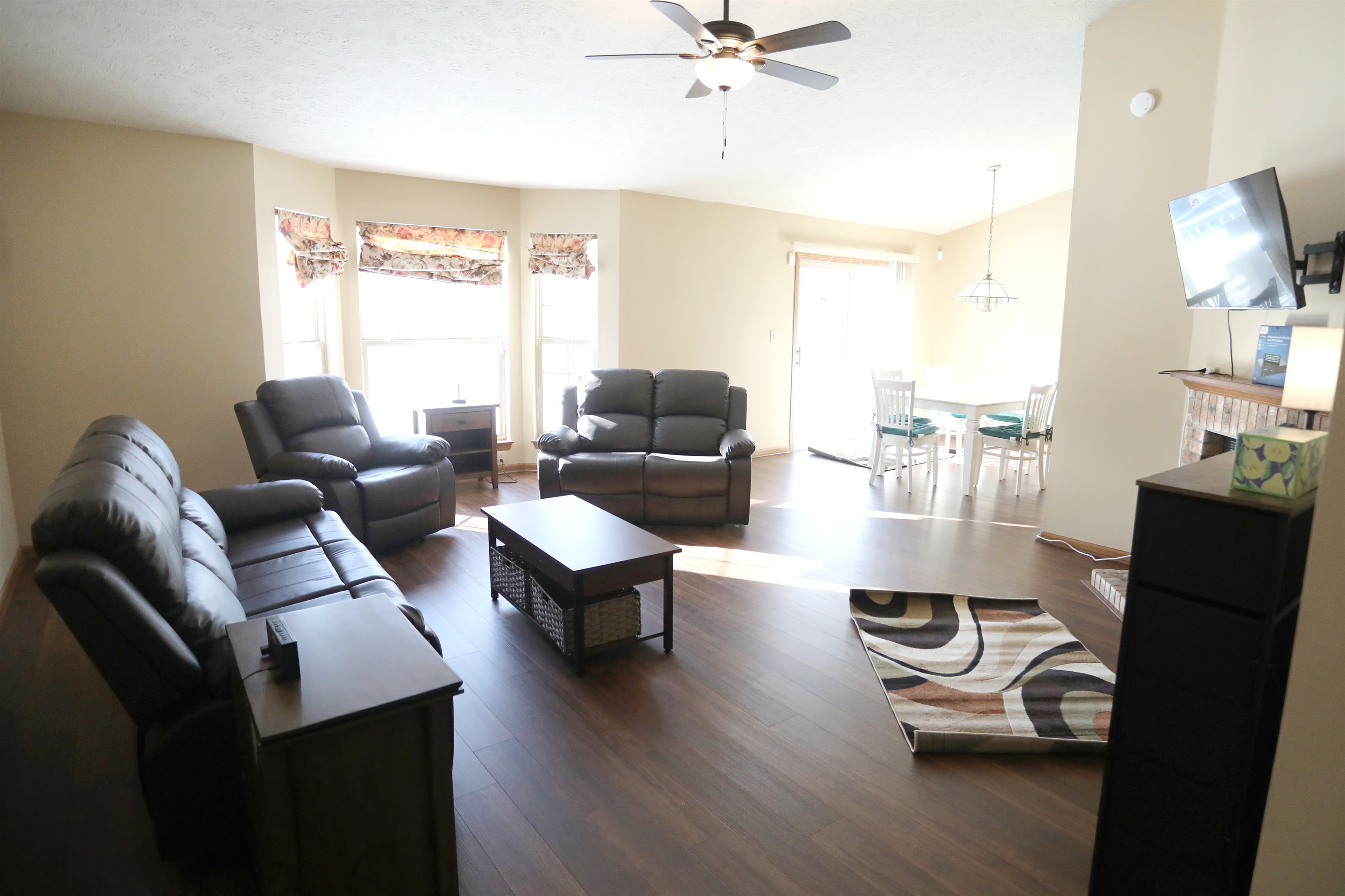 Living Room show Roku TV, fireplace, reclinable single seat, reclinable loveset, and reclinable sofa, coffee table, with dinette in the background
