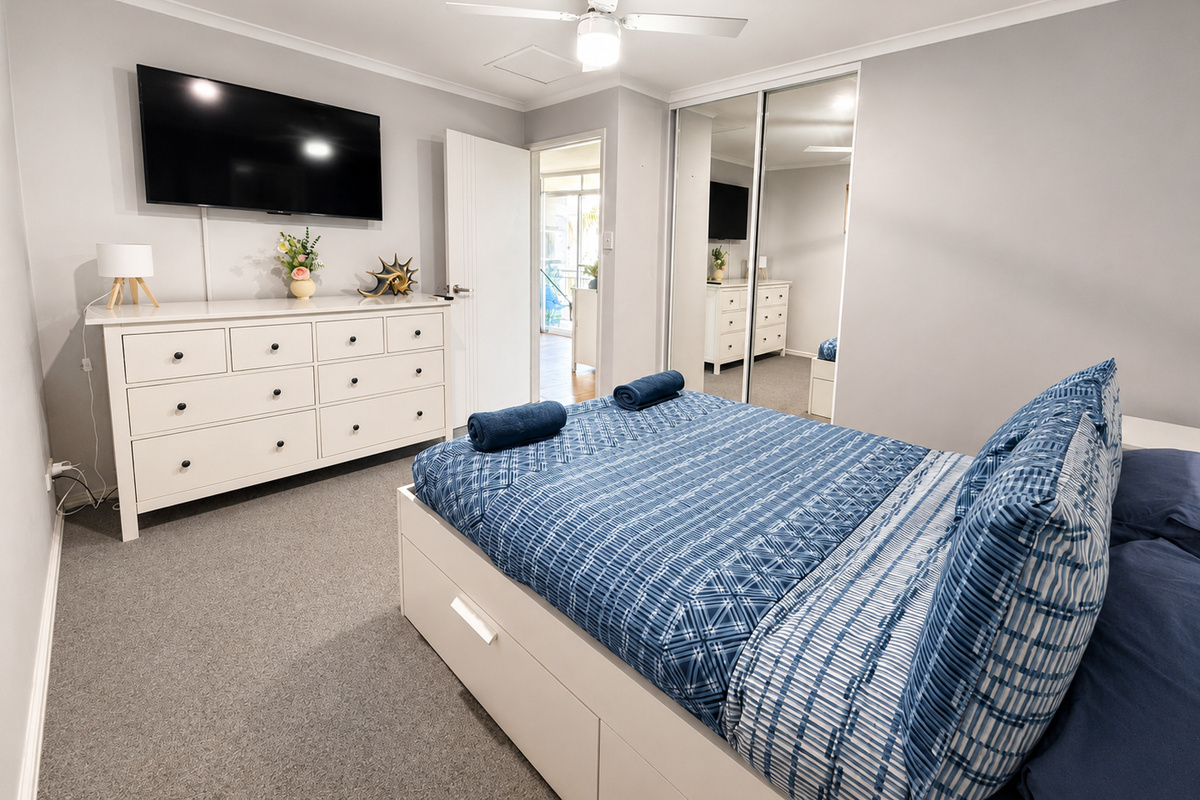 Tropical bedding, warm timber blinds and bedside lighting give the second bedroom a relaxed holiday feel inside Sea Breeze Apartment Mandurah.