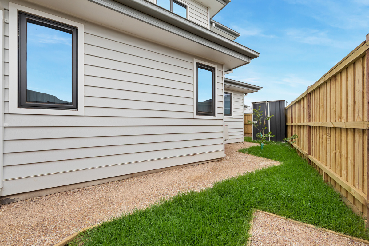Side of the home with a gravel path, lawn and fencing, giving a private outdoor strip beside the house.