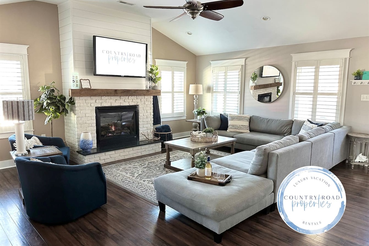 Relax in the bright, airy living room featuring a cozy white brick fireplace, a massive sectional, and stylish navy armchairs. It’s the ultimate space for family movie nights or wine by the fire during your dream getaway.