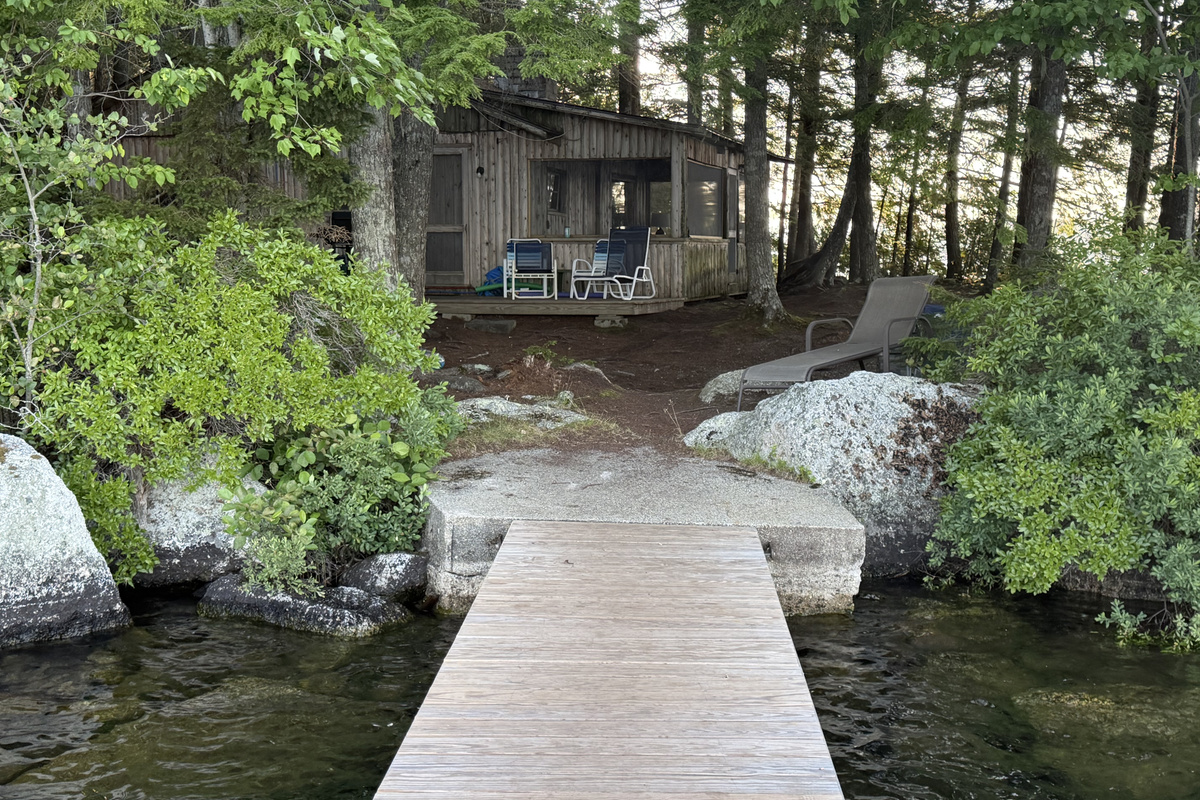 View looking back at camp standing on your private wooden dock! Steps off the concrete landing lead up natural granite rocks and pine paths to the deck and screened porch. Clear Beech Hill Pond water below—great spot to fish or launch kayaks!